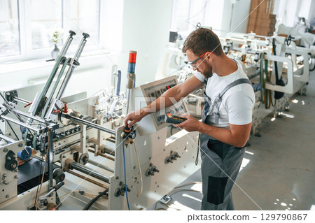 Standing by the machine. Handsome man is working at the factory of creating eco boxes 129790867
