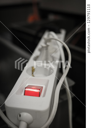 White electrical power strip with illuminated red switch and multiple outlets on a dark blurred 129791118