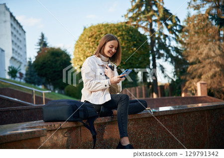 Cheerful, smiling. Young female student in casual clothes is outdoors 129791342