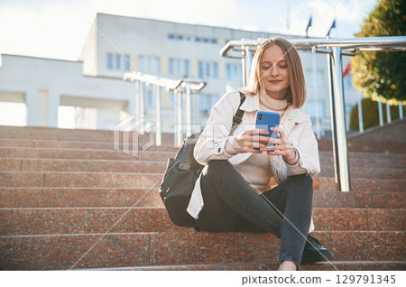 Smartphone in hands. Young female student in casual clothes is outdoors 129791345