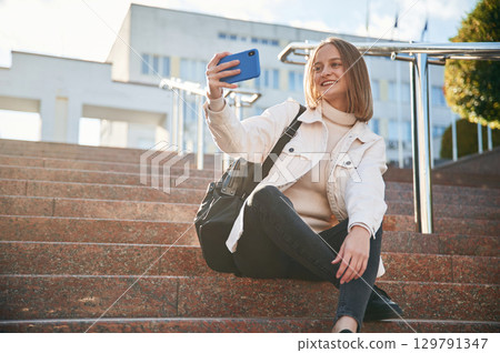 Making a selfie with smartphone. Young female student in casual clothes is outdoors 129791347
