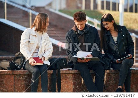 With notepad. Three young students are outside the university outdoors With notepad. Three young students are outside the university outdoors 129791417