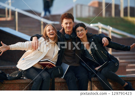 Embracing each other. Three young students are outside the university outdoors 129791423