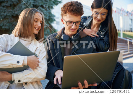 Sitting together. Three young students are outside the university outdoors 129791451