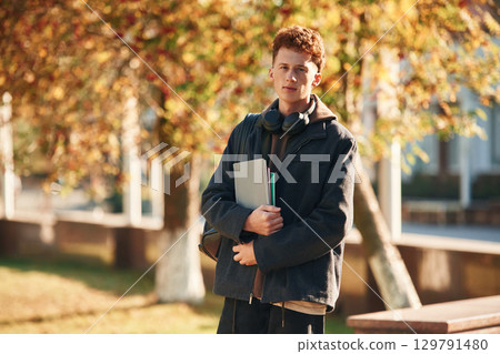 Standing and holding notepad. Young student is outside the university, in black clothes 129791480