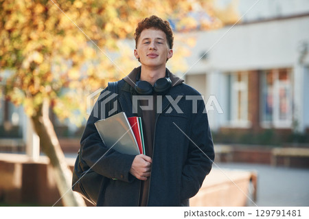 Standing and holding notepad. Young student is outside the university, in black clothes 129791481