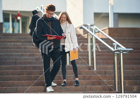 Front view, walking the stairs. Two young students are together outdoors Front view, walking the stairs. Two young students are together outdoors 129791504