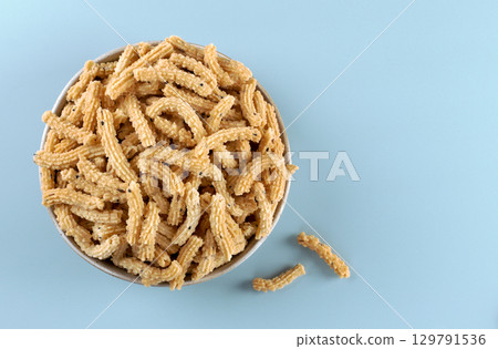 Traditional Indian snack murukku on blue background. Crispy treat made from rice flour and spices. Top view. Copy space 129791536