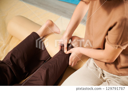 Masseuse making thai yoga massage. Cropped view of woman therapist doing traditional massage treatment for female patient indoors. Client lying on mat, enjoying hand massage. Close up. Masseuse making thai yoga massage. Cropped view of woman therapist doing traditional massage treatment for female patient indoors. Client lying on mat, enjoying hand massage. Close up. 129791787