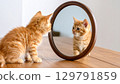 Curious orange kitten gazes into round mirror, captivated by its own reflection. warm wooden table adds cozy touch to scene, creating playful and charming atmosphere 129791859