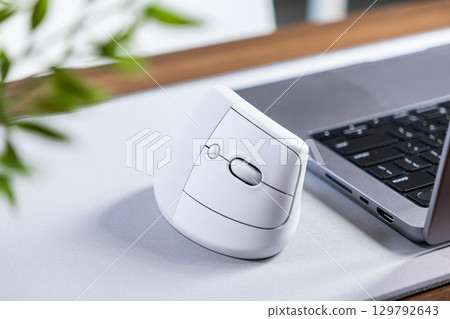 White ergonomic vertical mouse sits on a light grey desk mat, enhancing wrist comfort and promoting healthy posture for productive digital work White ergonomic vertical mouse sits on a light grey desk mat, enhancing wrist comfort and promoting healthy posture for productive digital work 129792643