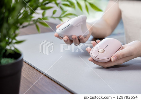 Hands comparing two distinct computer mice, a compact pink and an ergonomic vertical, illustrating modern tech choices for comfortable computing 129792654
