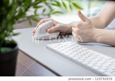Person's hand operating an ergonomic vertical mouse on a desk, giving a thumbs-up, promoting improved office comfort and digital efficiency Person's hand operating an ergonomic vertical mouse on a desk, giving a thumbs-up, promoting improved office comfort and digital efficiency 129792659