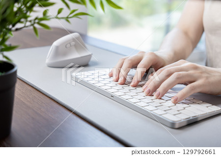 Female hands typing on a sleek keyboard with a white ergonomic vertical mouse, highlighting comfort and productivity in a modern remote work setup 129792661