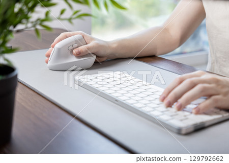 Person's hand operates a modern ergonomic vertical mouse and keyboard on a desk pad, emphasizing comfort and efficiency for prolonged remote work 129792662