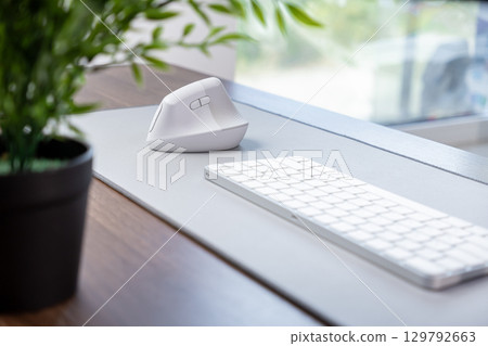 White ergonomic vertical mouse and minimalist keyboard on a grey desk mat, enhancing comfort, health, and productivity for a modern home office White ergonomic vertical mouse and minimalist keyboard on a grey desk mat, enhancing comfort, health, and productivity for a modern home office 129792663