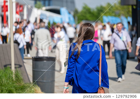 Woman walking in busy outdoor event with attendees and modern setting Woman walking in busy outdoor event with attendees and modern setting 129792906
