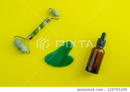 Bottle for cosmetics and jade massagers on a yellow background. Beauty saloon. Background with copy space. 129793209
