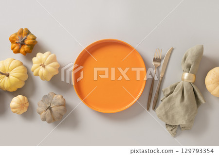 Autumn composition of colorful different small pumpkins, orange empty plate with golden cutlery on gray background. Harvest day, Concept catering or table setting. Top view. Thanksgiving Day. Banner. 129793354