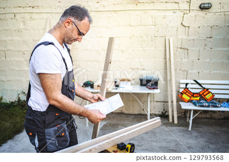 Mature male carpenter working with wooden plank outdoors 129793568