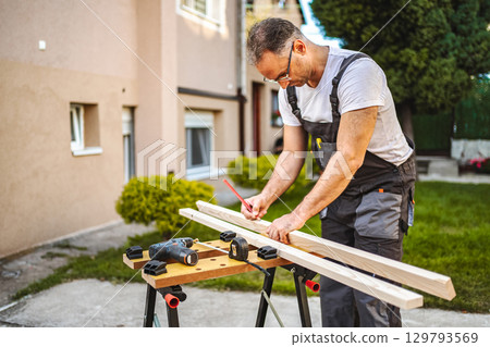 Mature male carpenter measuring wooden plank outdoors 129793569