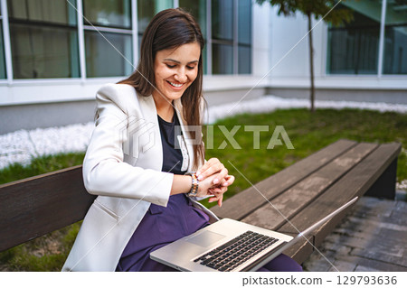 Businesswoman checking out time whille working on laptop outdoors Businesswoman checking out time whille working on laptop outdoors 129793636