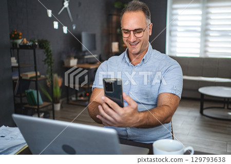 Middle aged Caucasian man using mobile phone and laptop at home Middle aged Caucasian man using mobile phone and laptop at home 129793638