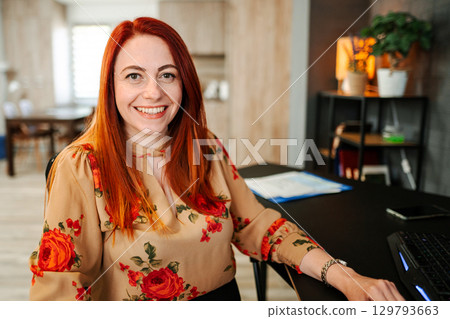 Portrait of a smiling red-haired woman at a desk Portrait of a smiling red-haired woman at a desk 129793663