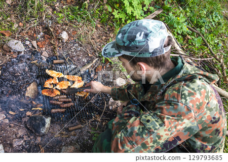 Soldier grilling chicken and sausages in the woods 129793685