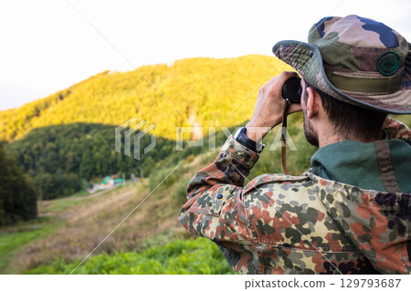Soldier observing enemy positions with binoculars in mountain forest Soldier observing enemy positions with binoculars in mountain forest 129793687
