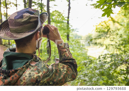 Soldier wearing camouflage uniform observing with binoculars in forest 129793688