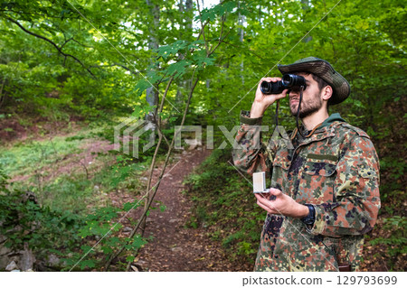 Forest ranger looking through binoculars while holding a compass Forest ranger looking through binoculars while holding a compass 129793699