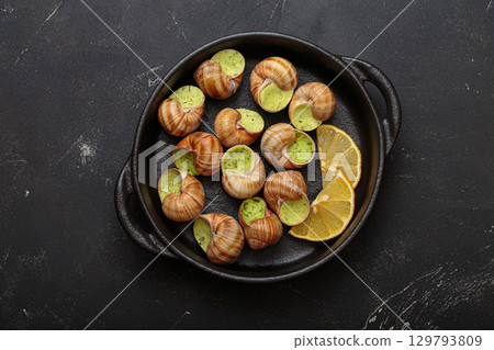 Snails escargots with garlic butter and lemon, served in a black pan on black rustic background Snails escargots with garlic butter and lemon, served in a black pan on black rustic background 129793809