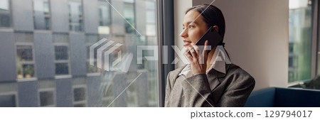 A Professional Woman Engaged in a Phone Conversation within a Modern Office Environment A Professional Woman Engaged in a Phone Conversation within a Modern Office Environment 129794017
