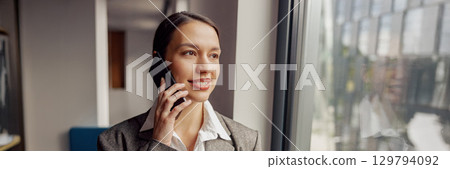 A Professional Woman Engaged in a Phone Call Within a Contemporary Office Environment A Professional Woman Engaged in a Phone Call Within a Contemporary Office Environment 129794092