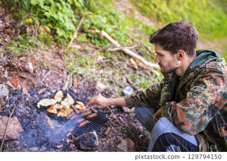 Hunter grilling meat and sausages in the woods 129794150