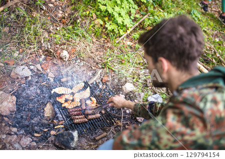 Soldier grilling meat and sausages over a campfire in the forest 129794154