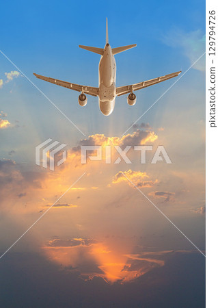 Passenger airplane flying into dramatic sunset sky 129794726