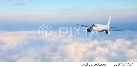 White passenger airplane flying above clouds at sunrise White passenger airplane flying above clouds at sunrise 129794734