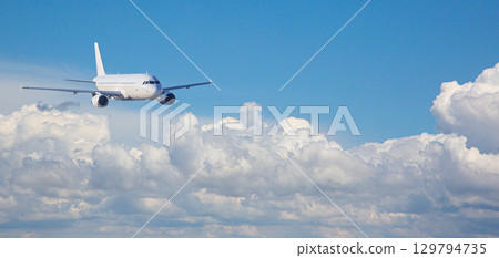 White passenger airplane flying above beautiful cloudscape on sunny day 129794735