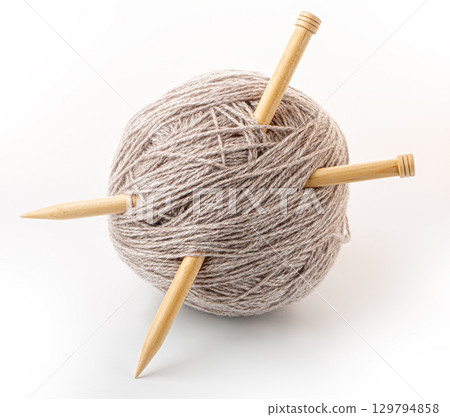 Two knitting needles crossing a ball of beige yarn on white background Two knitting needles crossing a ball of beige yarn on white background 129794858