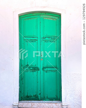 Old green wooden door on white wall with peeling paint 129794926