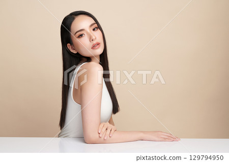 A beautiful young Asian woman with clean, fresh skin against a beige background. Skincare, facial treatment, cosmetology, beauty, and spa. An elegant portrait of an Asian woman. A beautiful young Asian woman with clean, fresh skin against a beige background. Skincare, facial treatment, cosmetology, beauty, and spa. An elegant portrait of an Asian woman. 129794950