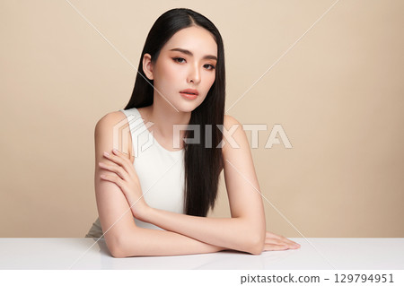 A beautiful young Asian woman with clean, fresh skin against a beige background. Skincare, facial treatment, cosmetology, beauty, and spa. An elegant portrait of an Asian woman. 129794951