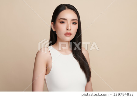 A beautiful young Asian woman with clean, fresh skin against a beige background. Skincare, facial treatment, cosmetology, beauty, and spa. An elegant portrait of an Asian woman. 129794952