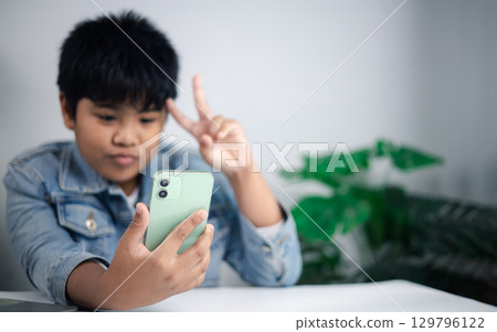 Youth lifestyle, self expression, digital communication, and the global impact of mobile technology and social media. Young person posing for a selfie with smartphone and peace sign. 129796122