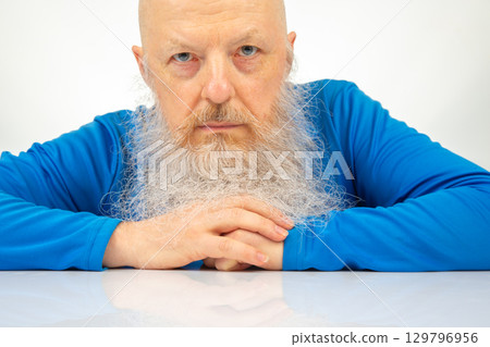 Older man with a long beard wearing a blue shirt and looking seriously at the camera indoors Older man with a long beard wearing a blue shirt and looking seriously at the camera indoors 129796956