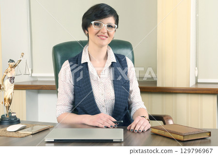 Professional woman at an office desk with laptop and law-themed decor Professional woman at an office desk with laptop and law-themed decor 129796967