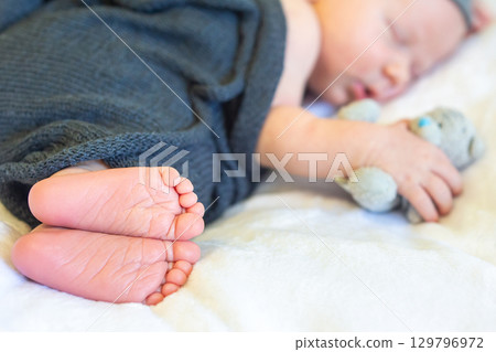 Baby peacefully sleeping while clutching a small toy in cozy surroundings 129796972