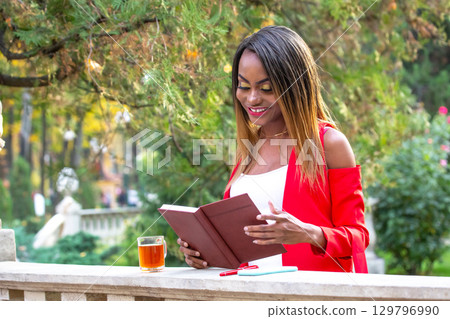 Woman enjoying a book while sipping tea in a beautiful garden setting 129796990